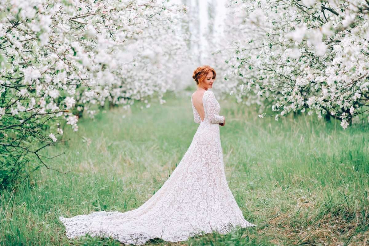 A young woman in a wedding dress is standing in a flowering spring garden.
