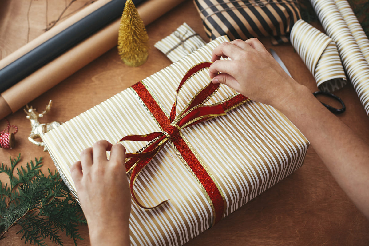 wrapping christmas gifts concept hands holding red ribbon wrapping stylish gift box striped golden paper scissors presents golden tree wooden table (1)